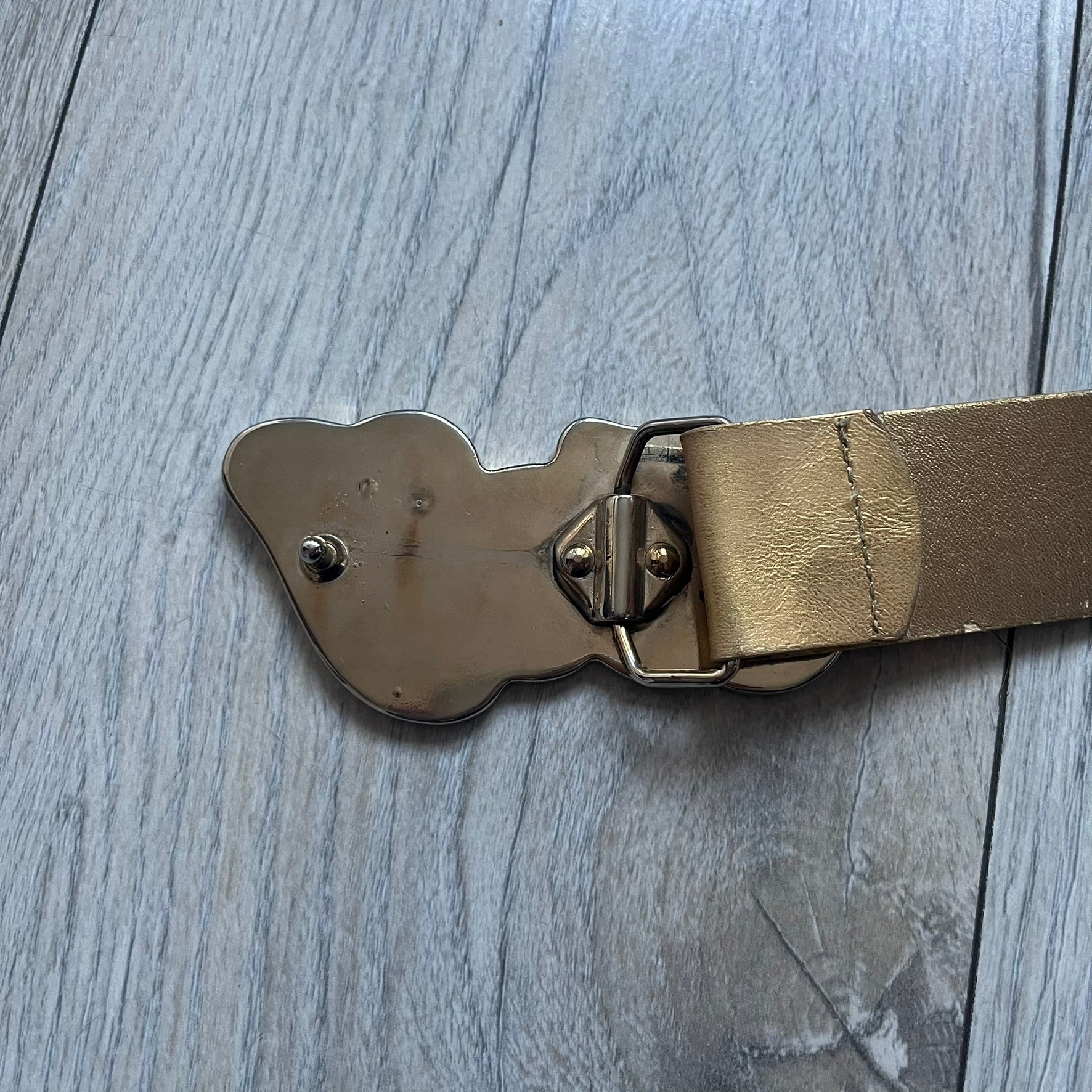 The Dolce & Gabbana 2000’s Gold Tone D&G Logo Belt is made from metallic gold leather and features a large D&G logo buckle shaped directly as the brand’s initials. The buckle uses a cursive D&G logo set over a glittery gold background, framed by a solid gold-tone metal outline. The entire buckle and belt maintain a consistent gold color scheme typical of Dolce & Gabbana accessories from the 2000s.