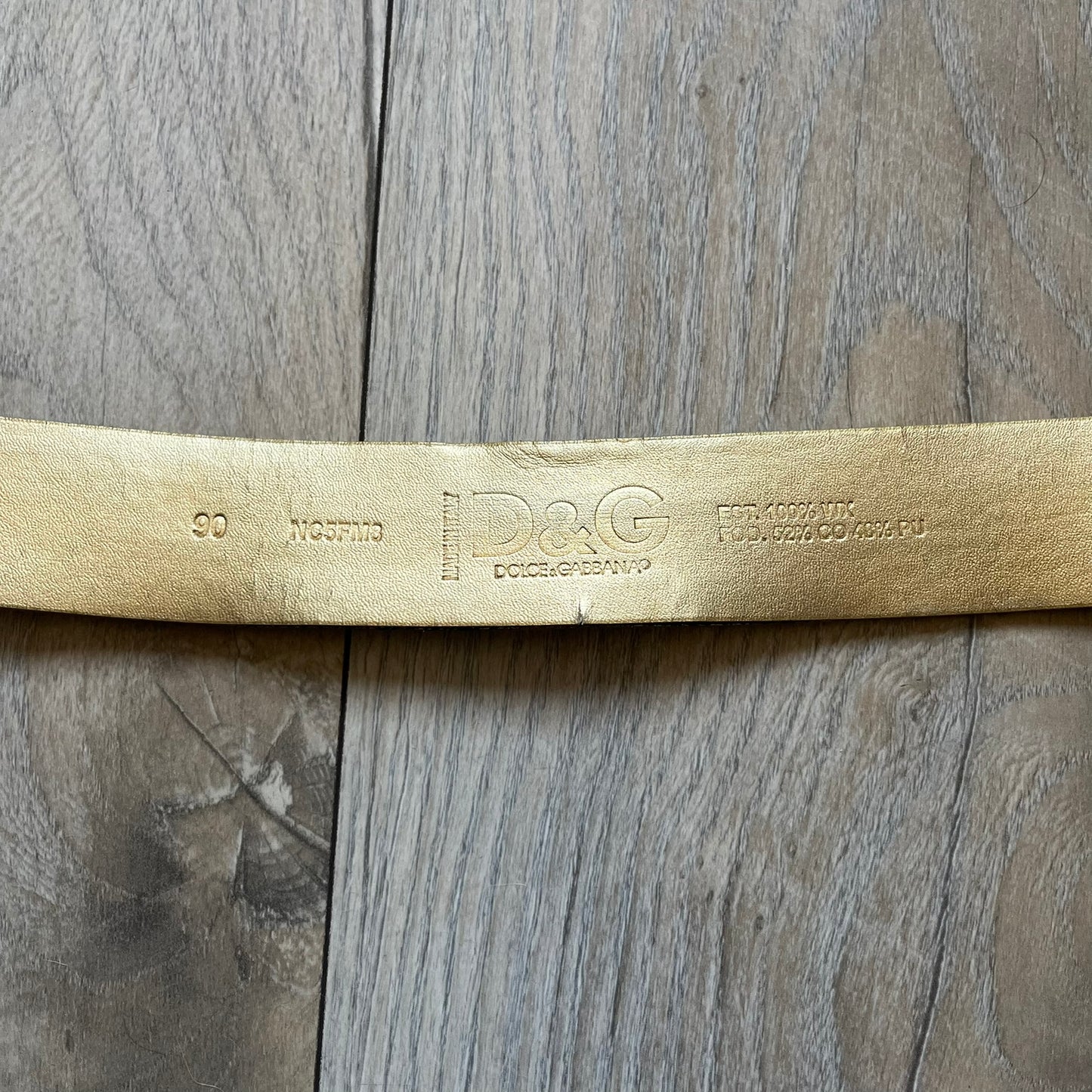 The Dolce &amp; Gabbana 2000’s Gold Tone D&amp;G Logo Belt is made from metallic gold leather and features a large D&amp;G logo buckle shaped directly as the brand’s initials. The buckle uses a cursive D&amp;G logo set over a glittery gold background, framed by a solid gold-tone metal outline. The entire buckle and belt maintain a consistent gold color scheme typical of Dolce &amp; Gabbana accessories from the 2000s.