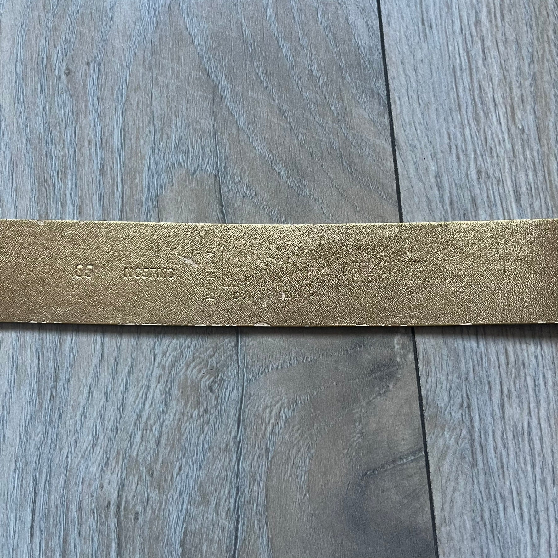 The Dolce & Gabbana 2000’s Gold Tone D&G Logo Belt is made from metallic gold leather and features a large D&G logo buckle shaped directly as the brand’s initials. The buckle uses a cursive D&G logo set over a glittery gold background, framed by a solid gold-tone metal outline. The entire buckle and belt maintain a consistent gold color scheme typical of Dolce & Gabbana accessories from the 2000s.