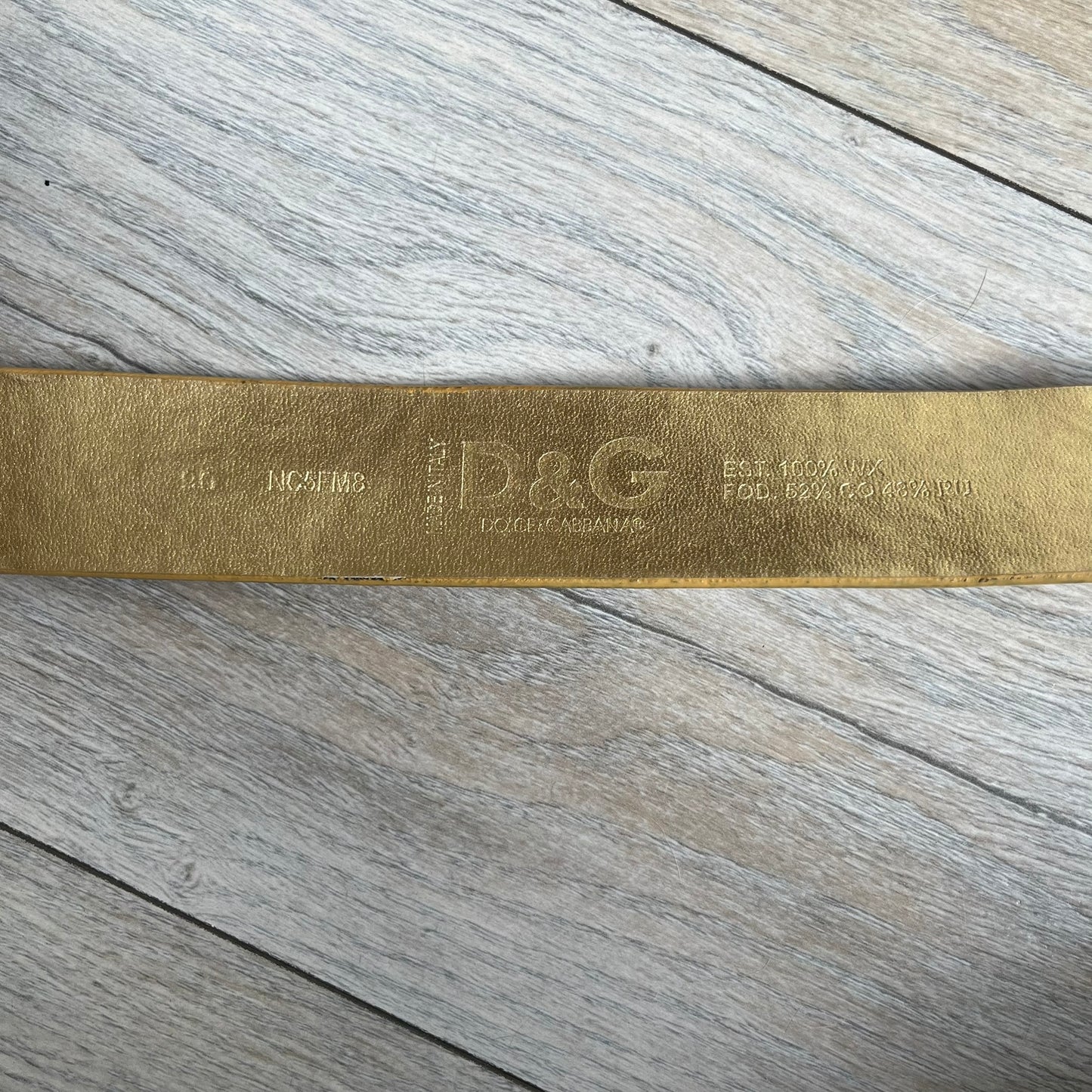 The Dolce &amp; Gabbana 2000’s Gold Tone D&amp;G Logo Belt is made from metallic gold leather and features a large D&amp;G logo buckle shaped directly as the brand’s initials. The buckle uses a cursive D&amp;G logo set over a glittery gold background, framed by a solid gold-tone metal outline. The entire buckle and belt maintain a consistent gold color scheme typical of Dolce &amp; Gabbana accessories from the 2000s.