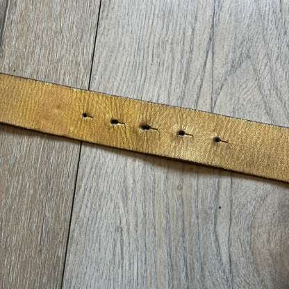 The Dolce &amp; Gabbana 2000’s Gold Tone D&amp;G Logo Belt is made from metallic gold leather and features a large D&amp;G logo buckle shaped directly as the brand’s initials. The buckle uses a cursive D&amp;G logo set over a glittery gold background, framed by a solid gold-tone metal outline. The entire buckle and belt maintain a consistent gold color scheme typical of Dolce &amp; Gabbana accessories from the 2000s.