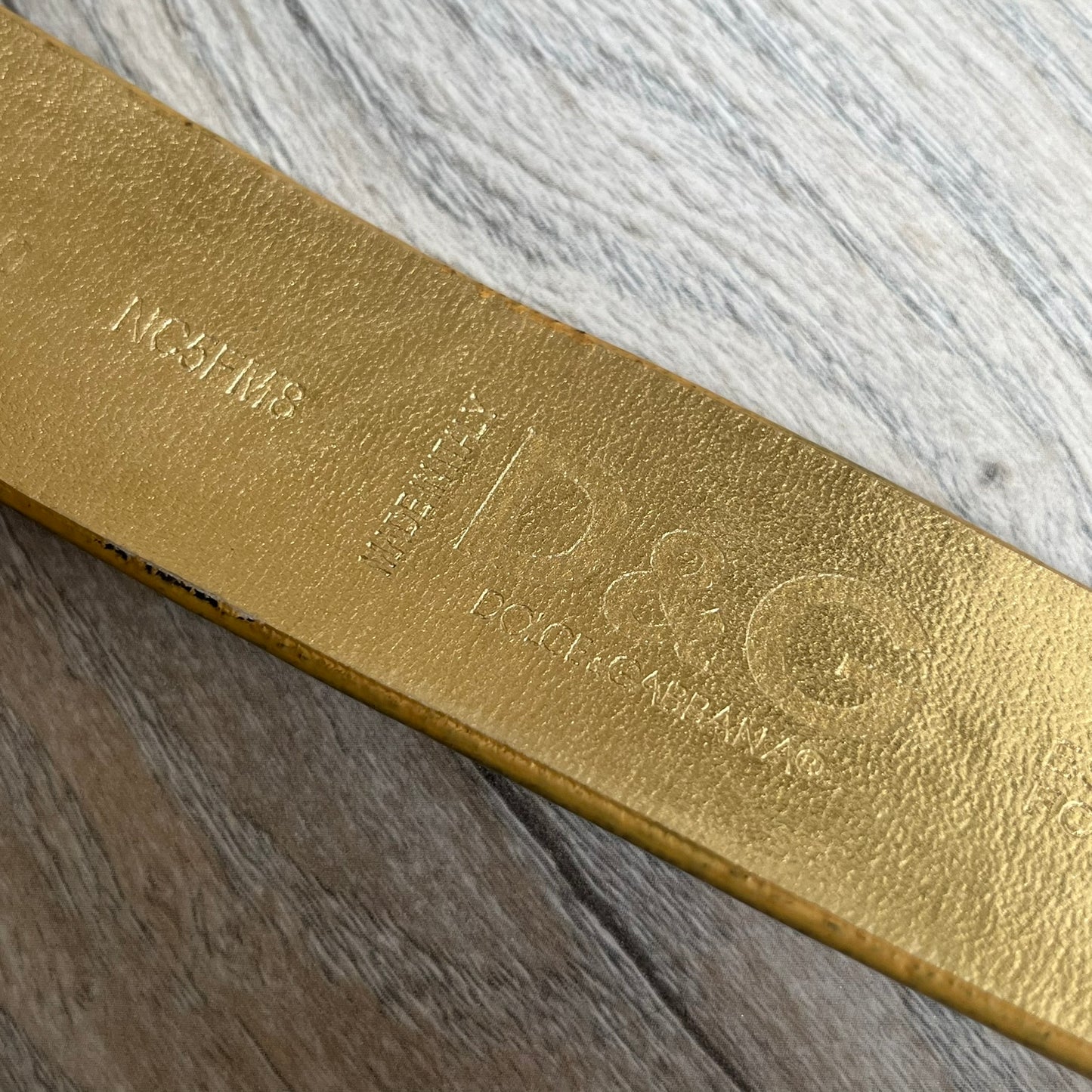 The Dolce &amp; Gabbana 2000’s Gold Tone D&amp;G Logo Belt is made from metallic gold leather and features a large D&amp;G logo buckle shaped directly as the brand’s initials. The buckle uses a cursive D&amp;G logo set over a glittery gold background, framed by a solid gold-tone metal outline. The entire buckle and belt maintain a consistent gold color scheme typical of Dolce &amp; Gabbana accessories from the 2000s.