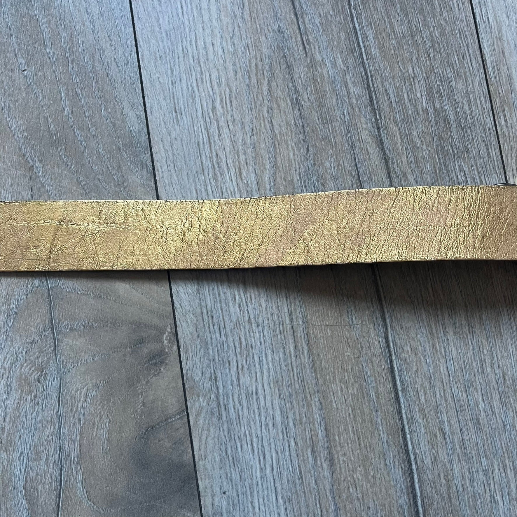 The Dolce & Gabbana 2000’s Gold Tone D&G Logo Belt is made from metallic gold leather and features a large D&G logo buckle shaped directly as the brand’s initials. The buckle uses a cursive D&G logo set over a glittery gold background, framed by a solid gold-tone metal outline. The entire buckle and belt maintain a consistent gold color scheme typical of Dolce & Gabbana accessories from the 2000s.