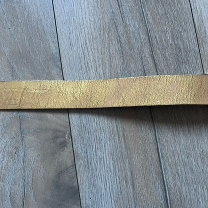 The Dolce & Gabbana 2000’s Gold Tone D&G Logo Belt is made from metallic gold leather and features a large D&G logo buckle shaped directly as the brand’s initials. The buckle uses a cursive D&G logo set over a glittery gold background, framed by a solid gold-tone metal outline. The entire buckle and belt maintain a consistent gold color scheme typical of Dolce & Gabbana accessories from the 2000s.