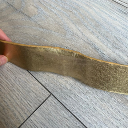 The Dolce &amp; Gabbana 2000’s Gold Tone D&amp;G Logo Belt is made from metallic gold leather and features a large D&amp;G logo buckle shaped directly as the brand’s initials. The buckle uses a cursive D&amp;G logo set over a glittery gold background, framed by a solid gold-tone metal outline. The entire buckle and belt maintain a consistent gold color scheme typical of Dolce &amp; Gabbana accessories from the 2000s.
