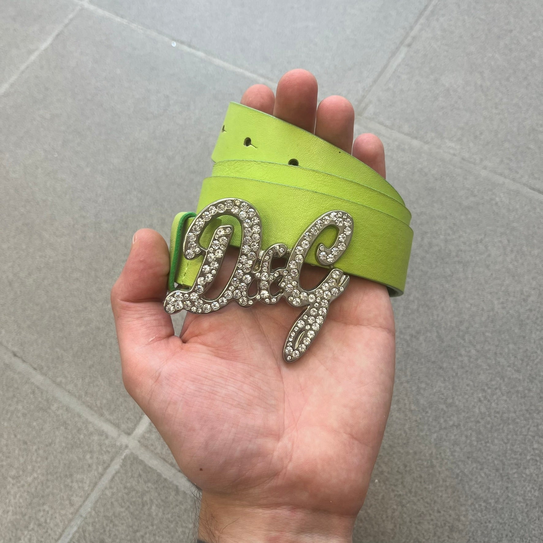 Dolce &amp; Gabbana 2000s Green Crystal Buckle Belt features a lime green leather strap with a stainless steel D&amp;G logo buckle. The buckle has a decorative italic-style font and is fully covered with crystal/rhinestone detailing on the front. Made in Italy.