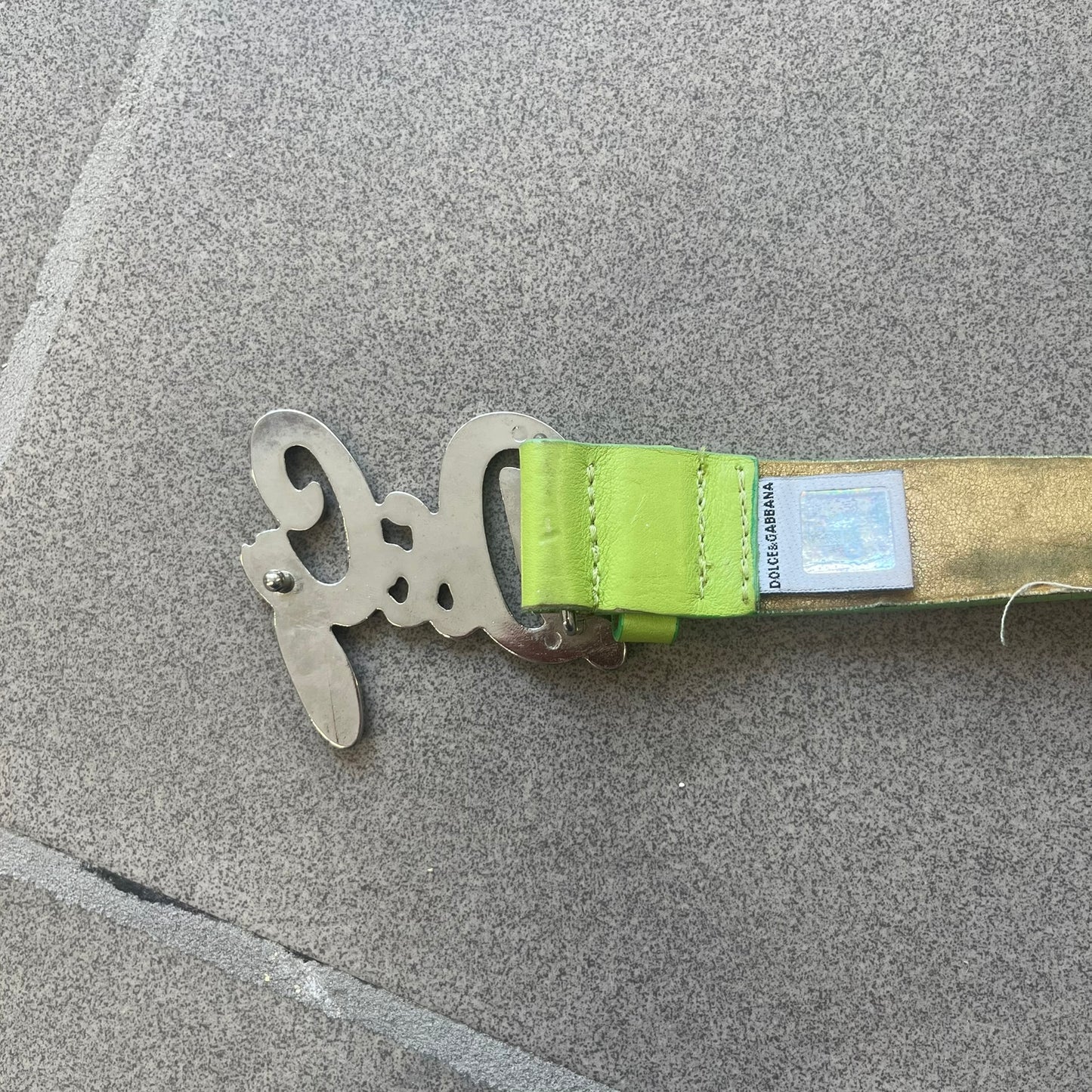 Dolce &amp; Gabbana 2000s Green Crystal Buckle Belt features a lime green leather strap with a stainless steel D&amp;G logo buckle. The buckle has a decorative italic-style font and is fully covered with crystal/rhinestone detailing on the front. Made in Italy.