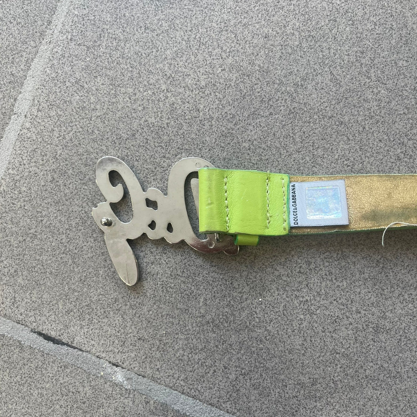 Dolce &amp; Gabbana 2000s Green Crystal Buckle Belt features a lime green leather strap with a stainless steel D&amp;G logo buckle. The buckle has a decorative italic-style font and is fully covered with crystal/rhinestone detailing on the front. Made in Italy.