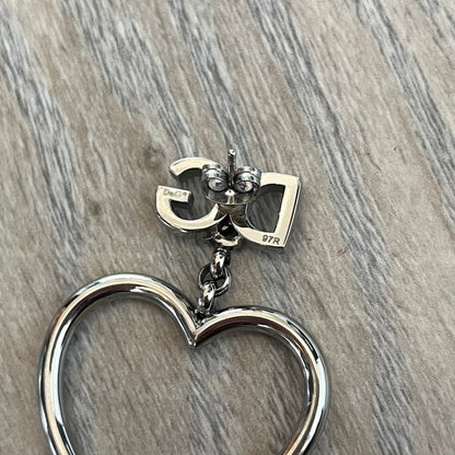 Dolce & Gabbana DJ1013 2000s Heart Earrings feature a silver-tone dangling design with D&G logo studs at the top and large outlined heart charms suspended below. The heart pendants are movable and hang freely from the logo attachment. The earrings come with the original Dolce & Gabbana dust bag.
