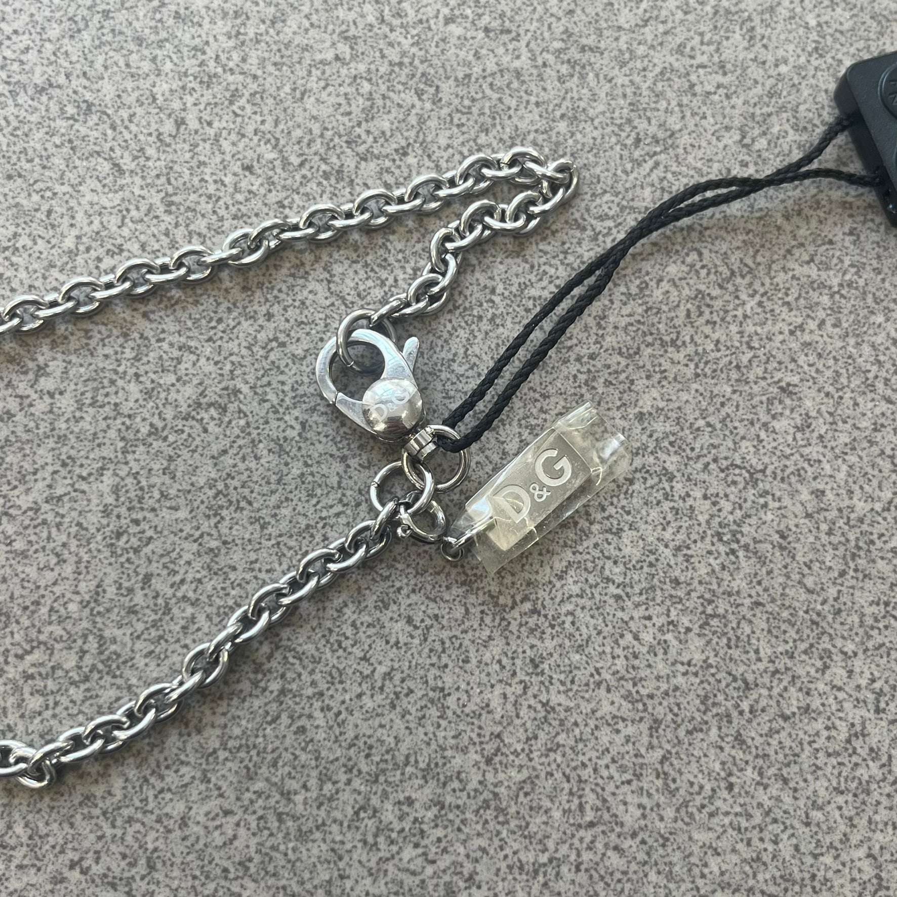 Dolce & Gabbana 2000s Horseshoe Necklace (DJ0985) is a stainless steel necklace featuring a horseshoe-shaped pendant. The pendant has a fixed section with a raised D&G logo, while the horseshoe portion is attached to it with a rotating design that allows it to spin freely. The necklace has a polished metal finish and comes from the 2000s.

