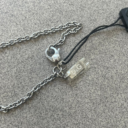 Dolce & Gabbana 2000s Horseshoe Necklace (DJ0985) is a stainless steel necklace featuring a horseshoe-shaped pendant. The pendant has a fixed section with a raised D&G logo, while the horseshoe portion is attached to it with a rotating design that allows it to spin freely. The necklace has a polished metal finish and comes from the 2000s.
