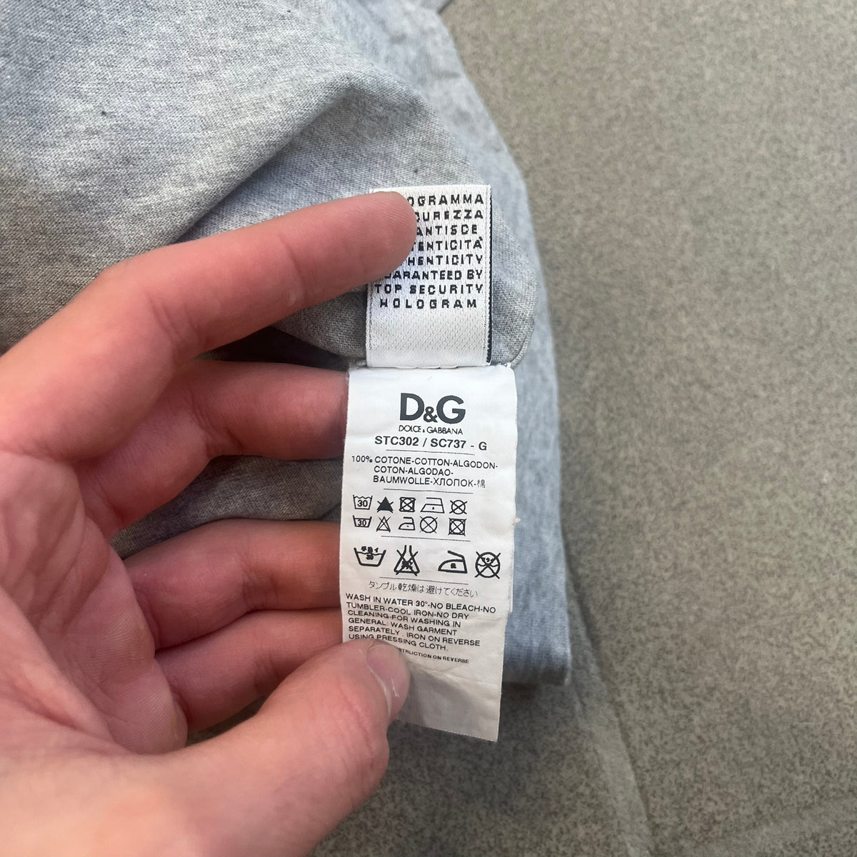 Dolce &amp; Gabbana 2000's Kim Basinger Tee is a gray T-shirt with a photo of Kim Basinger on the front and small “Herb Ritts Foundation” text below it. The lower back has D&amp;G text logo. The shirt is constructed inside-out style, with the stitching visible along the sides.