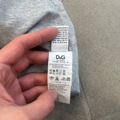Dolce &amp; Gabbana 2000's Kim Basinger Tee is a gray T-shirt with a photo of Kim Basinger on the front and small “Herb Ritts Foundation” text below it. The lower back has D&amp;G text logo. The shirt is constructed inside-out style, with the stitching visible along the sides.