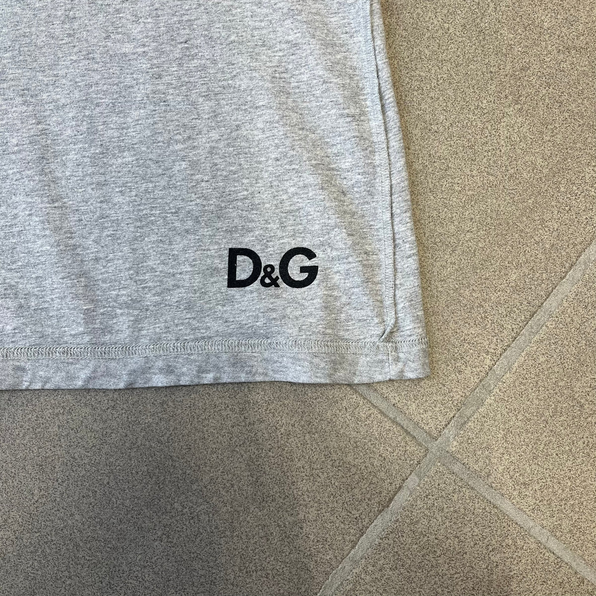 Dolce &amp; Gabbana 2000's Kim Basinger Tee is a gray T-shirt with a photo of Kim Basinger on the front and small “Herb Ritts Foundation” text below it. The lower back has D&amp;G text logo. The shirt is constructed inside-out style, with the stitching visible along the sides.