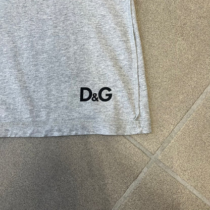Dolce &amp; Gabbana 2000's Kim Basinger Tee is a gray T-shirt with a photo of Kim Basinger on the front and small “Herb Ritts Foundation” text below it. The lower back has D&amp;G text logo. The shirt is constructed inside-out style, with the stitching visible along the sides.