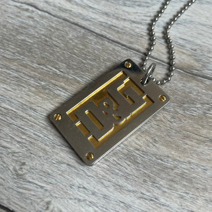 Dolce &amp; Gabbana 2000s Layered Gold/Silver Necklace DJ0721 is a chain necklace featuring a steel ball chain with lobster clasp engraved with D&amp;G branding. The pendant is constructed in a layered design with three sections: a gold-tone middle layer and silver-tone top and bottom layers. The front and back includes a cut-out D&amp;G logo with an outlined frame