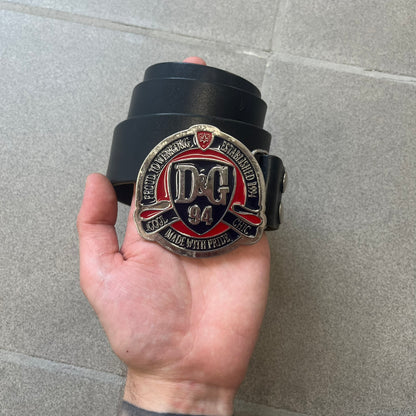 Dolce &amp; Gabbana "Made with Pride" Belt features a circular silver buckle with D&amp;G 94 at the center, surrounded by “Proud to Wear D&amp;G,” “Made with Pride,” and “Established 1994” text. Finished with subtle red and navy accents, it comes with a non-D&amp;G basic black leather belt.