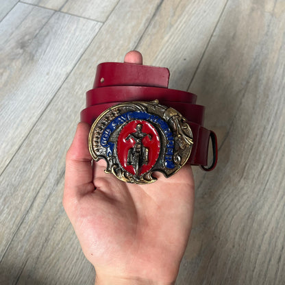 Dolce & Gabbana 2000s Moto Biker Leather Belt is a dark red leather belt made in Italy. The bronze-tone buckle features blue and red enamel detailing, with a biker graphic in the center on a red background. Above the rider is “GOD SAVE THE RIDER” text on a blue background. The buckle is finished with star detailing. Made from 100% leather.
