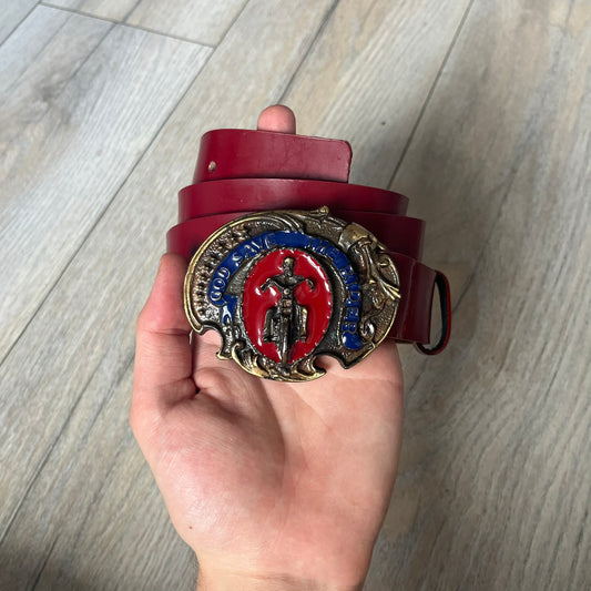 Dolce & Gabbana 2000s Moto Biker Leather Belt is a dark red leather belt made in Italy. The bronze-tone buckle features blue and red enamel detailing, with a biker graphic in the center on a red background. Above the rider is “GOD SAVE THE RIDER” text on a blue background. The buckle is finished with star detailing. Made from 100% leather.