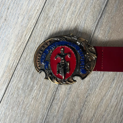 Dolce & Gabbana 2000s Moto Biker Leather Belt is a dark red leather belt made in Italy. The bronze-tone buckle features blue and red enamel detailing, with a biker graphic in the center on a red background. Above the rider is “GOD SAVE THE RIDER” text on a blue background. The buckle is finished with star detailing. Made from 100% leather.