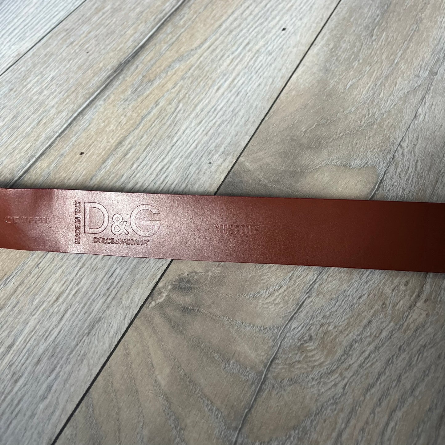 Dolce & Gabbana 2000s Moto Biker Leather Belt is a dark red leather belt made in Italy. The bronze-tone buckle features blue and red enamel detailing, with a biker graphic in the center on a red background. Above the rider is “GOD SAVE THE RIDER” text on a blue background. The buckle is finished with star detailing. Made from 100% leather.
