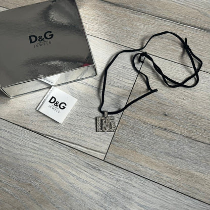 Dolce &amp; Gabbana 2000s Overlap Logo Necklace DJ0530 is a necklace featuring a pendant with overlapping D&amp;G letter cutouts in a slightly raised 3D design. The front is flooded with crystals/rhinestones. The back of the pendant is flat with a small engraved D&amp;G logo. It is attached to an adjustable cord chain with a regulator closure.
