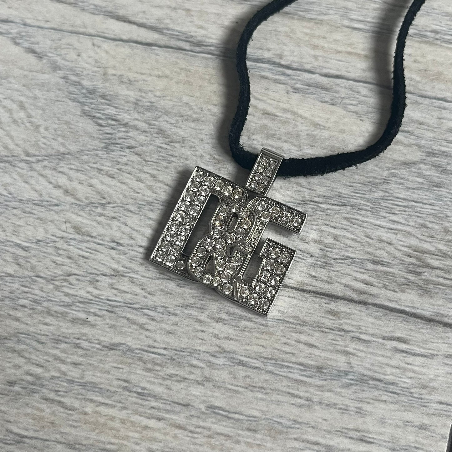 Dolce &amp; Gabbana 2000s Overlap Logo Necklace DJ0530 is a necklace featuring a pendant with overlapping D&amp;G letter cutouts in a slightly raised 3D design. The front is flooded with crystals/rhinestones. The back of the pendant is flat with a small engraved D&amp;G logo. It is attached to an adjustable cord chain with a regulator closure.
