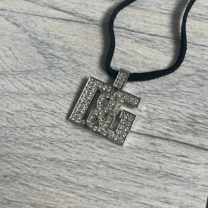 Dolce &amp; Gabbana 2000s Overlap Logo Necklace DJ0530 is a necklace featuring a pendant with overlapping D&amp;G letter cutouts in a slightly raised 3D design. The front is flooded with crystals/rhinestones. The back of the pendant is flat with a small engraved D&amp;G logo. It is attached to an adjustable cord chain with a regulator closure.
