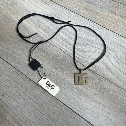Dolce & Gabbana 2000s Overlap Logo Necklace DJ0530 is a necklace featuring a pendant with overlapping D&G letter cutouts in a slightly raised 3D design. The back of the pendant is flat with a small engraved D&G logo. It is attached to an adjustable cord chain with a regulator closure.
