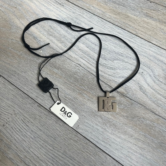Dolce & Gabbana 2000s Overlap Logo Necklace DJ0530 is a necklace featuring a pendant with overlapping D&G letter cutouts in a slightly raised 3D design. The back of the pendant is flat with a small engraved D&G logo. It is attached to an adjustable cord chain with a regulator closure.
