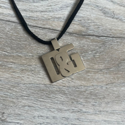 Dolce & Gabbana 2000s Overlap Logo Necklace DJ0530 is a necklace featuring a pendant with overlapping D&G letter cutouts in a slightly raised 3D design. The back of the pendant is flat with a small engraved D&G logo. It is attached to an adjustable cord chain with a regulator closure.
