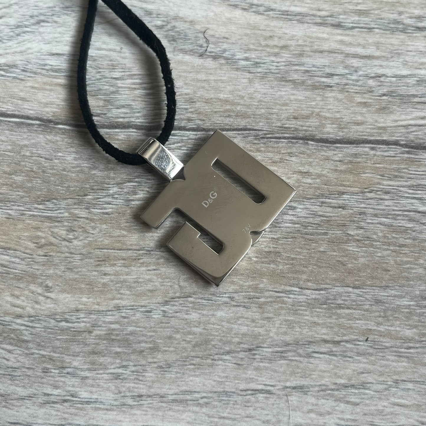 Dolce & Gabbana 2000s Overlap Logo Necklace DJ0530 is a necklace featuring a pendant with overlapping D&G letter cutouts in a slightly raised 3D design. The back of the pendant is flat with a small engraved D&G logo. It is attached to an adjustable cord chain with a regulator closure.
