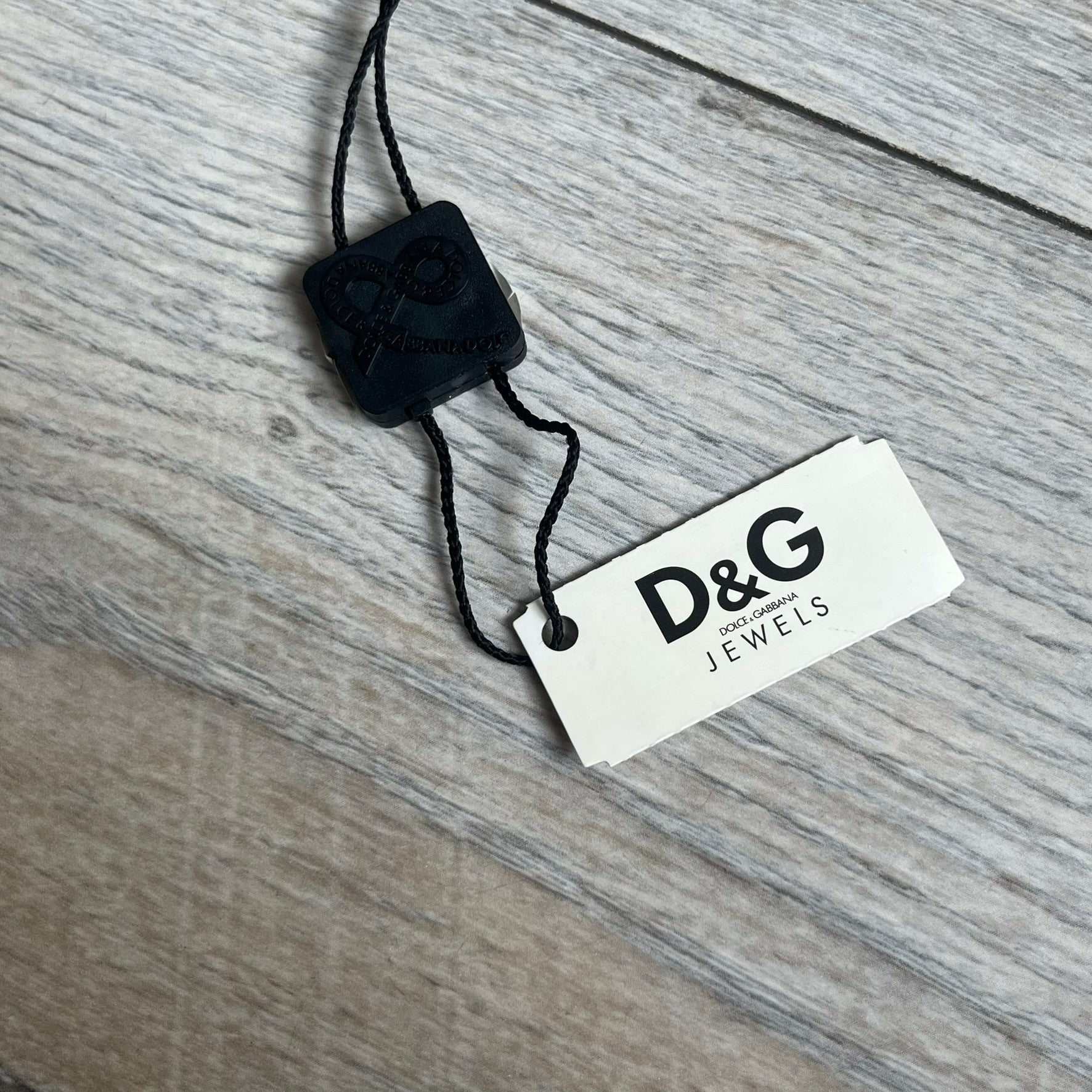 Dolce & Gabbana 2000s Overlap Logo Necklace DJ0530 is a necklace featuring a pendant with overlapping D&G letter cutouts in a slightly raised 3D design. The back of the pendant is flat with a small engraved D&G logo. It is attached to an adjustable cord chain with a regulator closure.
