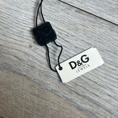 Dolce & Gabbana 2000s Overlap Logo Necklace DJ0530 is a necklace featuring a pendant with overlapping D&G letter cutouts in a slightly raised 3D design. The back of the pendant is flat with a small engraved D&G logo. It is attached to an adjustable cord chain with a regulator closure.
