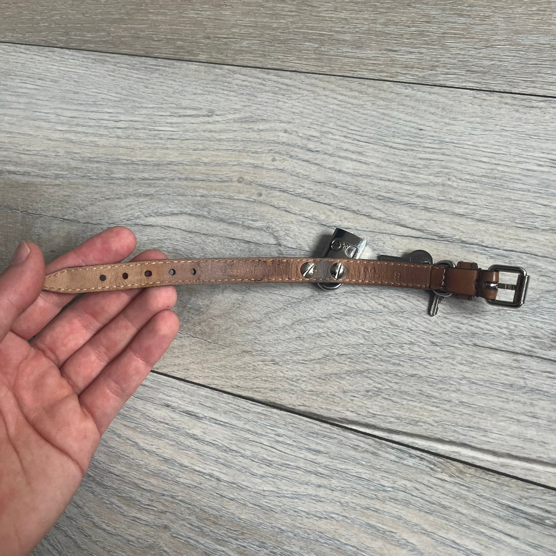 Dolce & Gabbana 2000s Padlock Leather Bracelet is a brown leather bracelet with an adjustable closure and multiple sizing holes. It features two metal loops, with a D&G engraved padlock attached to one loop and two metal keys attached to the other. The bracelet comes with its original box.
