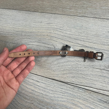 Dolce & Gabbana 2000s Padlock Leather Bracelet is a brown leather bracelet with an adjustable closure and multiple sizing holes. It features two metal loops, with a D&G engraved padlock attached to one loop and two metal keys attached to the other. The bracelet comes with its original box.

