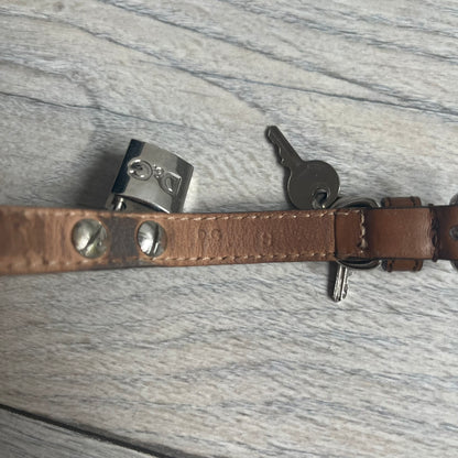 Dolce & Gabbana 2000s Padlock Leather Bracelet is a brown leather bracelet with an adjustable closure and multiple sizing holes. It features two metal loops, with a D&G engraved padlock attached to one loop and two metal keys attached to the other. The bracelet comes with its original box.
