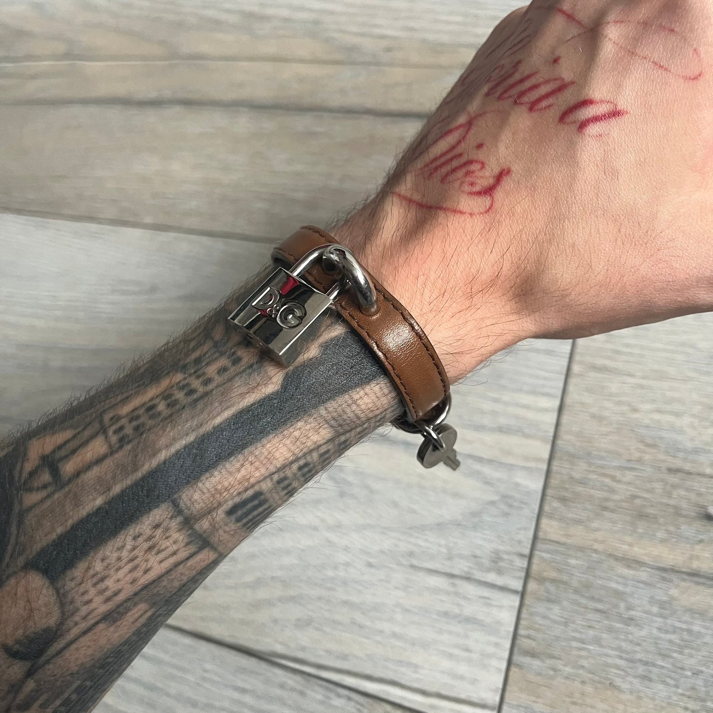 Dolce & Gabbana 2000s Padlock Leather Bracelet is a brown leather bracelet with an adjustable closure and multiple sizing holes. It features two metal loops, with a D&G engraved padlock attached to one loop and two metal keys attached to the other. The bracelet comes with its original box.
