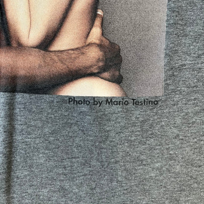 ● Dolce &amp; Gabbana 2000's Photo by Mario Testino Tee is a gray T-shirt with a photo of Naked Man and Woman holding each other on the front, and small “Photo by Mario Testino” text below it. The upper back has “D&amp;G 10 La Roue De La Fortune” text. The shirt is constructed inside-out style, with the stitching visible along the sides.