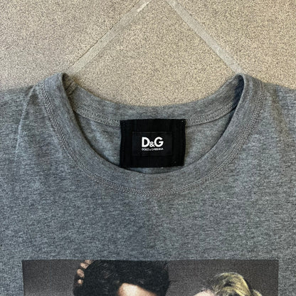 ● Dolce &amp; Gabbana 2000's Photo by Mario Testino Tee is a gray T-shirt with a photo of Naked Man and Woman holding each other on the front, and small “Photo by Mario Testino” text below it. The upper back has “D&amp;G 10 La Roue De La Fortune” text. The shirt is constructed inside-out style, with the stitching visible along the sides.