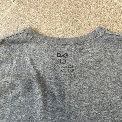 Dolce &amp; Gabbana 2000's Photo by Mario Testino Tee is a gray T-shirt with a photo of Naked Man and Woman holding each other on the front, and small “Photo by Mario Testino” text below it. The upper back has “D&amp;G 10 La Roue De La Fortune” text. The shirt is constructed inside-out style, with the stitching visible along the sides.