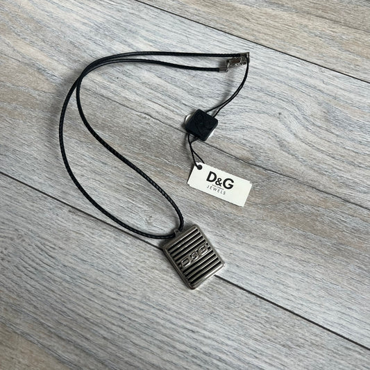 Dolce & Gabbana 2000s Radiator Necklace DJ0705 is a necklace featuring a square-link chain combined with a black leather cord. The pendant is made from stainless steel with a square frame design that includes black and silver line detailing resembling a radiator structure. A raised D&G logo is positioned in the center of the ID plate, while the back is black, visible through the open metal line design.