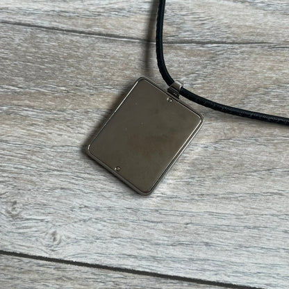 Dolce & Gabbana 2000s Radiator Necklace DJ0705 is a necklace featuring a square-link chain combined with a black leather cord. The pendant is made from stainless steel with a square frame design that includes black and silver line detailing resembling a radiator structure. A raised D&G logo is positioned in the center of the ID plate, while the back is black, visible through the open metal line design.