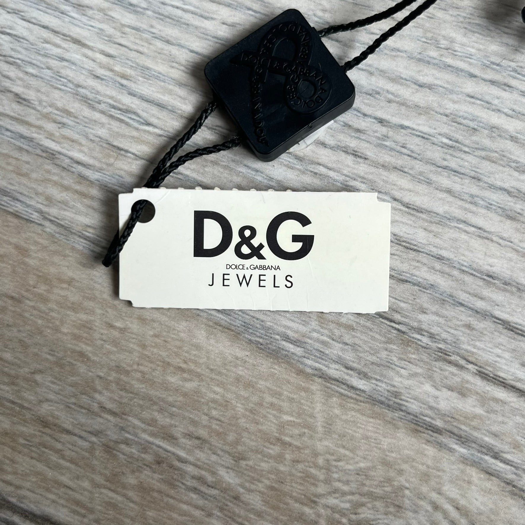 Dolce & Gabbana 2000s Radiator Necklace DJ0705 is a necklace featuring a square-link chain combined with a black leather cord. The pendant is made from stainless steel with a square frame design that includes black and silver line detailing resembling a radiator structure. A raised D&G logo is positioned in the center of the ID plate, while the back is black, visible through the open metal line design.