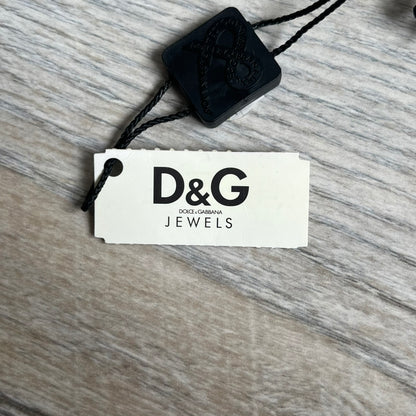 Dolce & Gabbana 2000s Radiator Necklace DJ0705 is a necklace featuring a square-link chain combined with a black leather cord. The pendant is made from stainless steel with a square frame design that includes black and silver line detailing resembling a radiator structure. A raised D&G logo is positioned in the center of the ID plate, while the back is black, visible through the open metal line design.