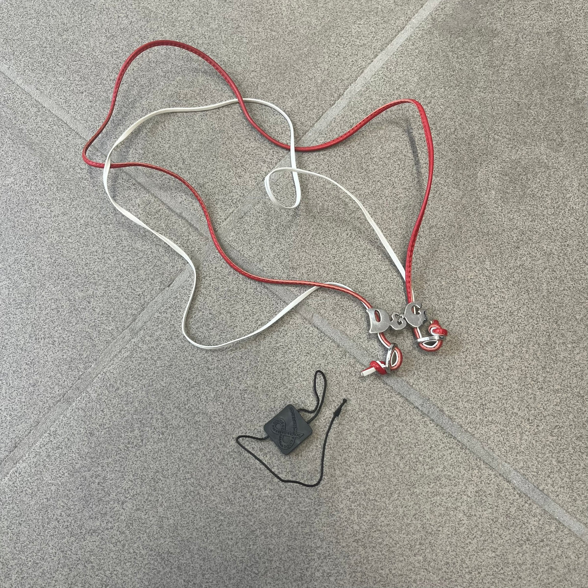 Dolce &amp; Gabbana 2000s Red &amp; White Strings Necklace &amp; Bracelet is a versatile accessory featuring red and white leather cords joined with stainless steel end caps. The center is finished with a stainless steel D&amp;G logo, while the back of the logo features a small engraved D&amp;G mark. Designed to be worn either as a necklace or wrapped as a bracelet.