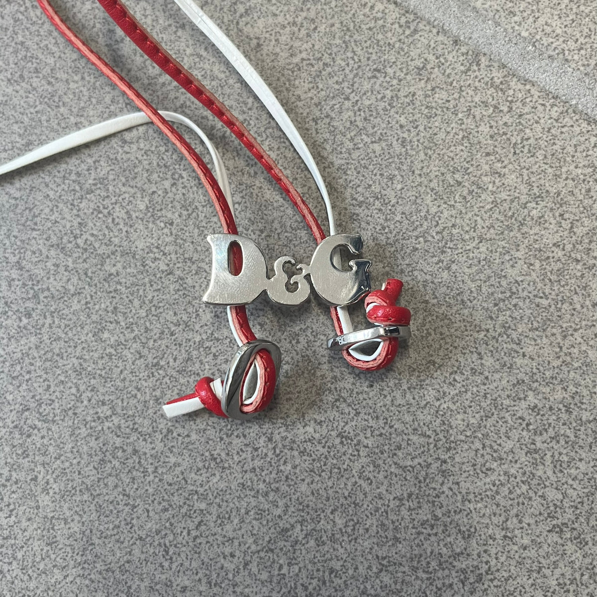 Dolce &amp; Gabbana 2000s Red &amp; White Strings Necklace &amp; Bracelet is a versatile accessory featuring red and white leather cords joined with stainless steel end caps. The center is finished with a stainless steel D&amp;G logo, while the back of the logo features a small engraved D&amp;G mark. Designed to be worn either as a necklace or wrapped as a bracelet.