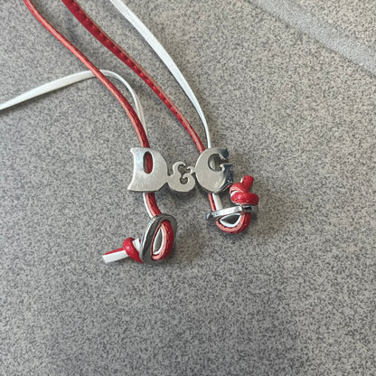 Dolce &amp; Gabbana 2000s Red &amp; White Strings Necklace &amp; Bracelet is a versatile accessory featuring red and white leather cords joined with stainless steel end caps. The center is finished with a stainless steel D&amp;G logo, while the back of the logo features a small engraved D&amp;G mark. Designed to be worn either as a necklace or wrapped as a bracelet.
