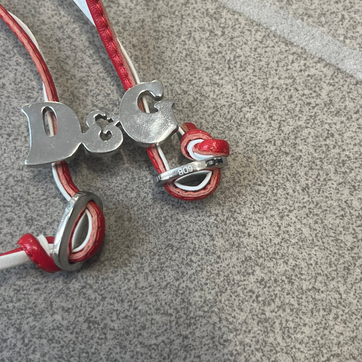 Dolce &amp; Gabbana 2000s Red &amp; White Strings Necklace &amp; Bracelet is a versatile accessory featuring red and white leather cords joined with stainless steel end caps. The center is finished with a stainless steel D&amp;G logo, while the back of the logo features a small engraved D&amp;G mark. Designed to be worn either as a necklace or wrapped as a bracelet.