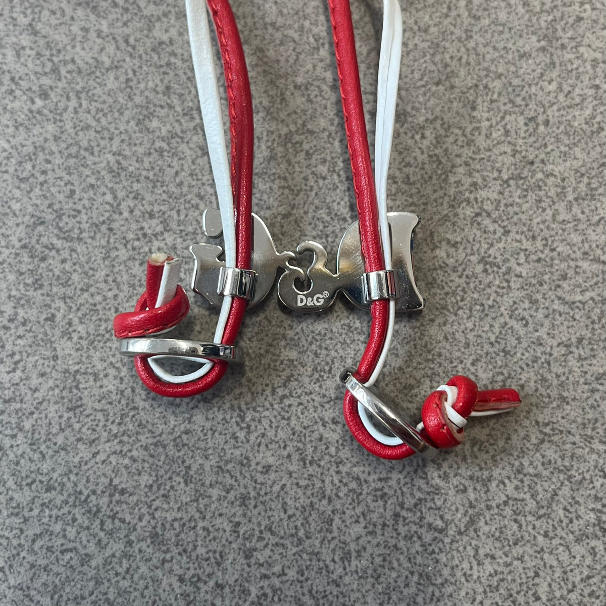 Dolce &amp; Gabbana 2000s Red &amp; White Strings Necklace &amp; Bracelet is a versatile accessory featuring red and white leather cords joined with stainless steel end caps. The center is finished with a stainless steel D&amp;G logo, while the back of the logo features a small engraved D&amp;G mark. Designed to be worn either as a necklace or wrapped as a bracelet.